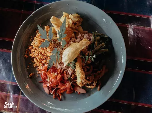 Spiced Sri Lankan rice and vegetables in a blue bowl with fresh herbs and papad, served on a striped tablecloth