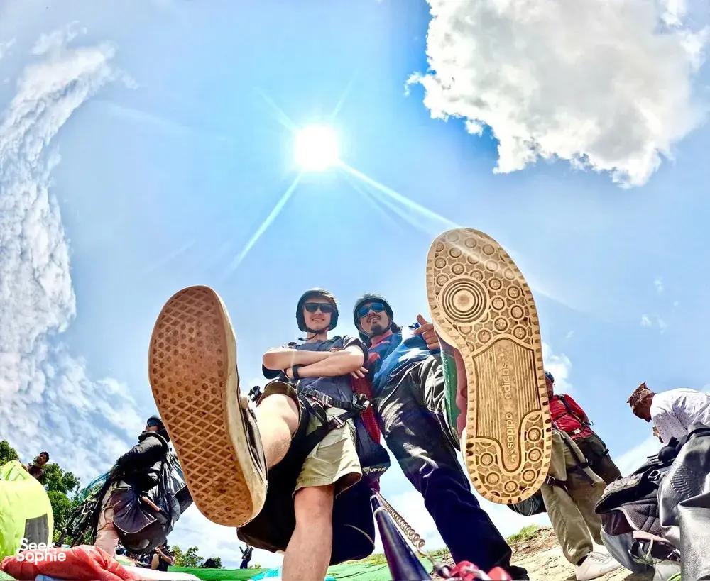 Paragliding team basking in the sun during take-off with multiple riders’ shoes and harnesses visible against blue sky, Sapa