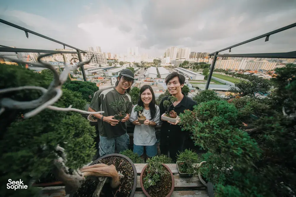 Three people smiling while holding bonsai pots on a terrace during a Japanese-style tropical bonsai workshop in Singapore