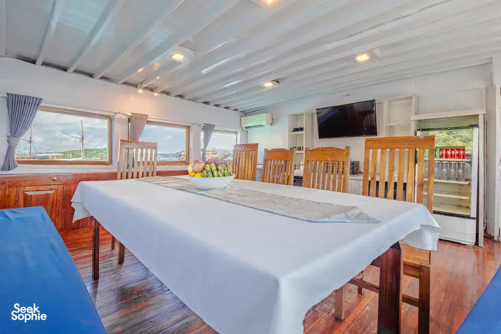 Boat dining room with pressed tables and windows, set for guests during a 3-day join-in Komodo boat trip in Labuan Bajo