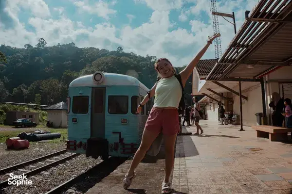 Passenger posing beside a turquoise carriage at a jungle railway platform in Sabah on Xtreme Paddlers’ jungle train
