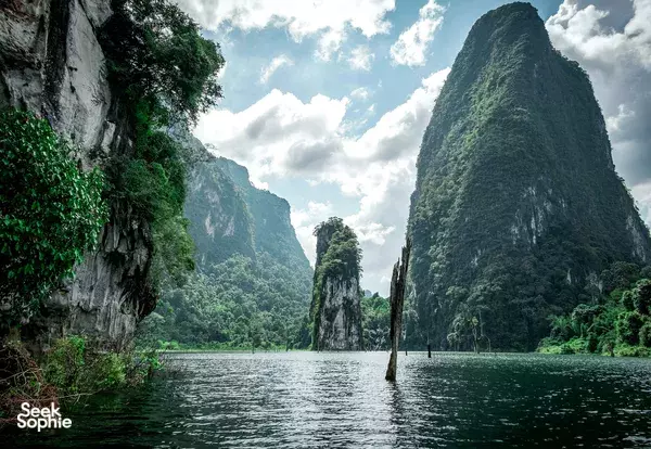 Calm lake surrounded by towering limestone cliffs in Thailand, with lush jungle covering the valley sides