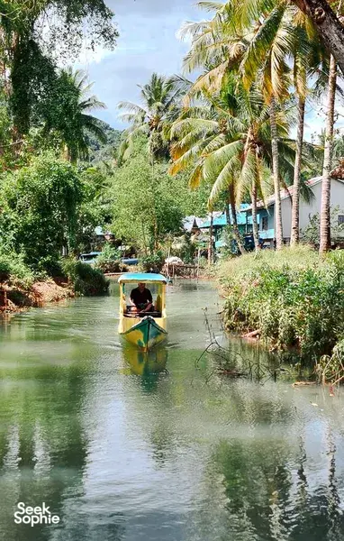 Passenger paddling along a narrow mangrove channel beneath palm trees on a day trip exploring hidden waterways in Labuan Bajo