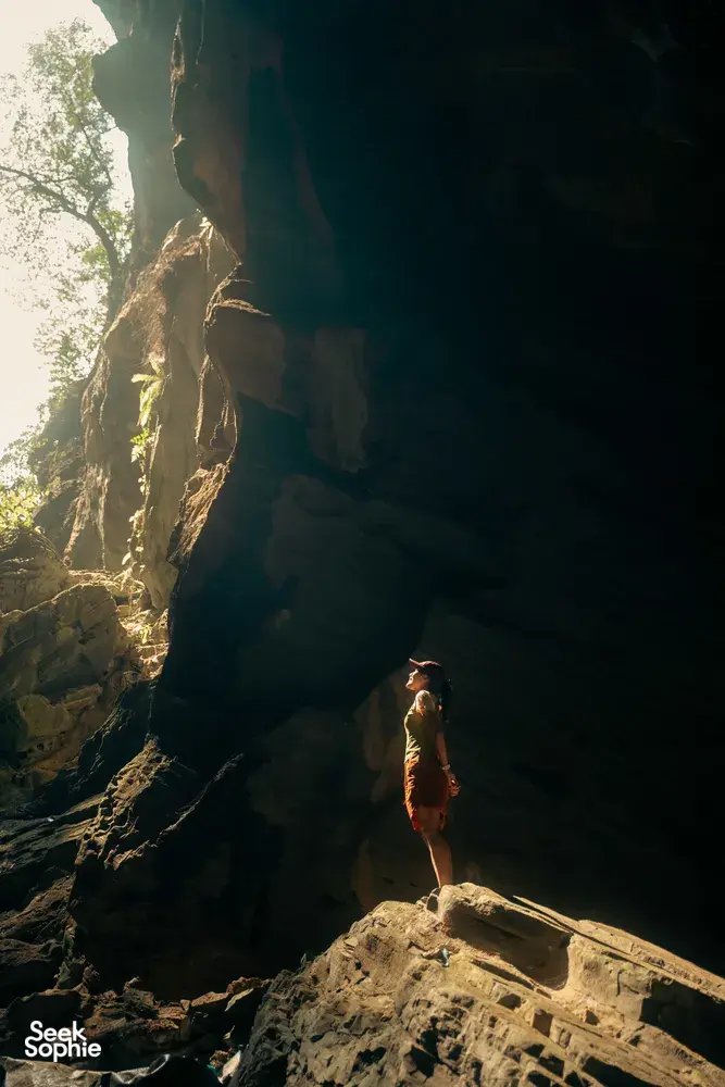 Cave trekker on a rocky ledge inside Phong Nha-Kẻ Bàng cave, looking toward daylight on a Greenland Tours visit