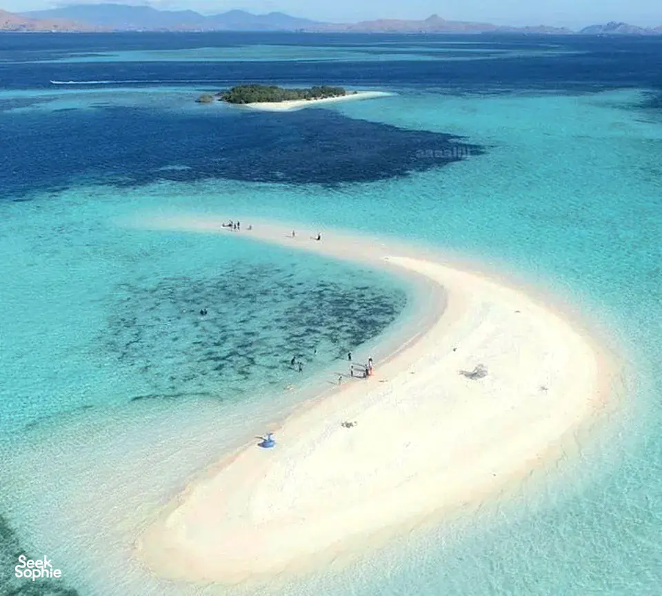 Aerial view of turquoise water and a crescent sand beach with boats and islets on a 3D2N shared Komodo cruise — Komodo Island