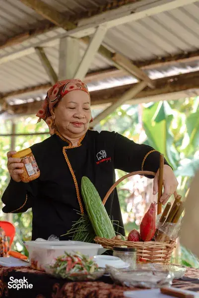 Indigenous Sabahan family cook holding a spice jar at a wooden table outdoors in Kota Kinabalu, Sabah
