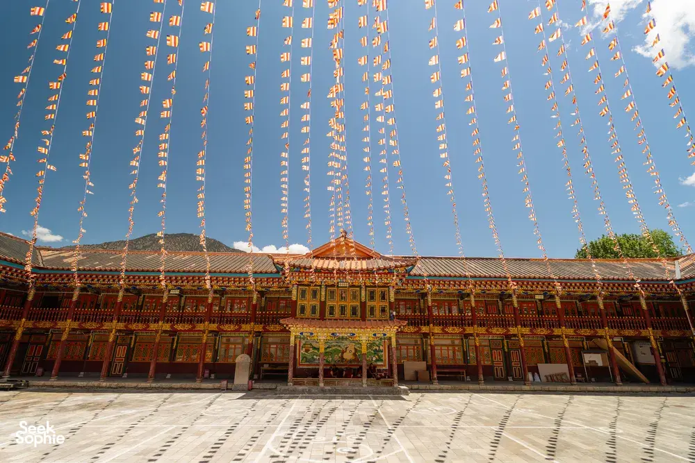 Ornate monastery facade in Shangri-La covered with fluttering prayer flags, warm sunlight over patterned courtyard walls