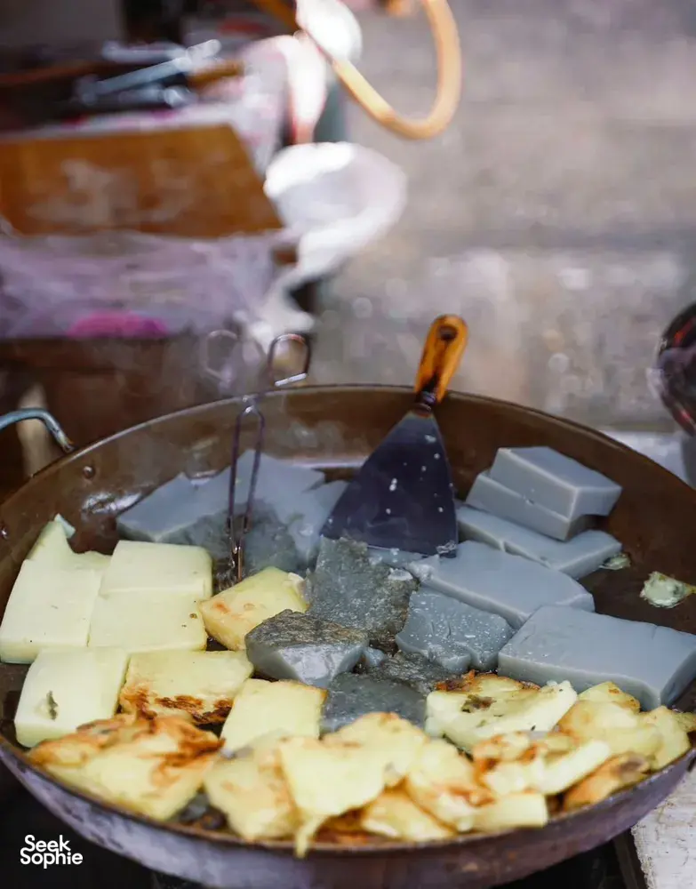 Smoky street-food wok in Lijiang with cubed foods sizzling over charcoal at a street stall during a local food hunt
