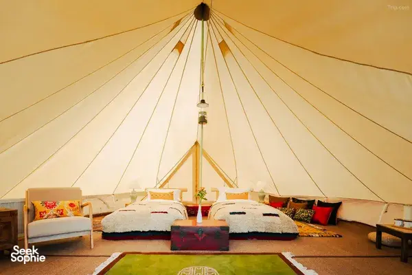 Glamping tent interior at Ferme Liotard in Shangri-La with two covered beds, central rug and a hanging light under canvas