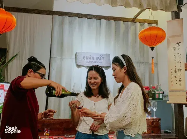 Guests at Chan Dat Living Room in Hoi An pouring and tasting red wine, smiling with glasses in a lantern-lit room