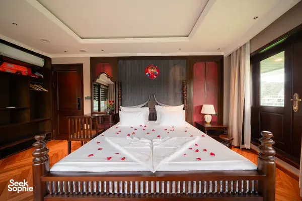 Luxe cruise bedroom with king bed, rose‑petal towel swan decoration, built-in wardrobe and curtains, Cat Ba 2D1N
