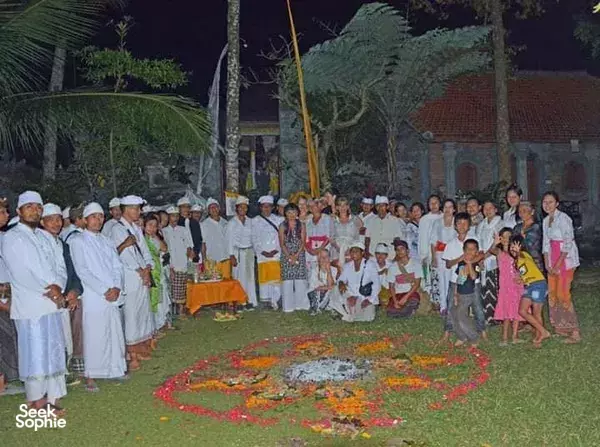 Participants in white ceremonial clothing gather around a flower mandala for a sacred ritual in the garden at Omunity Bali, Bali