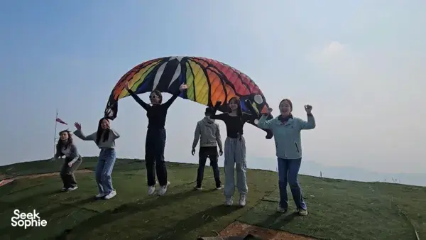Tandem paragliding group on a grassy launch hill in Hanoi, colourful canopy open above as they prepare for take-off