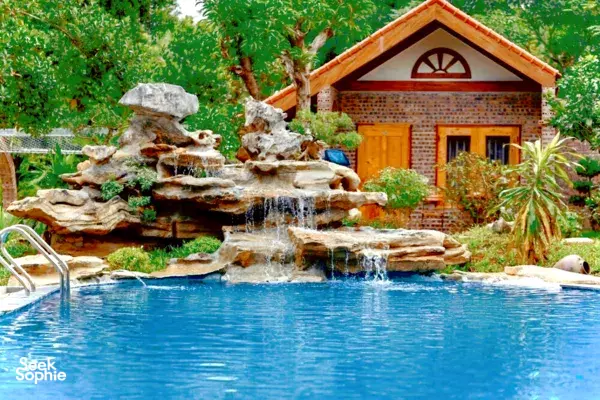 Stone water fountain and cascading waterfall beside a blue pool in the garden of a Ninh Binh village homestay