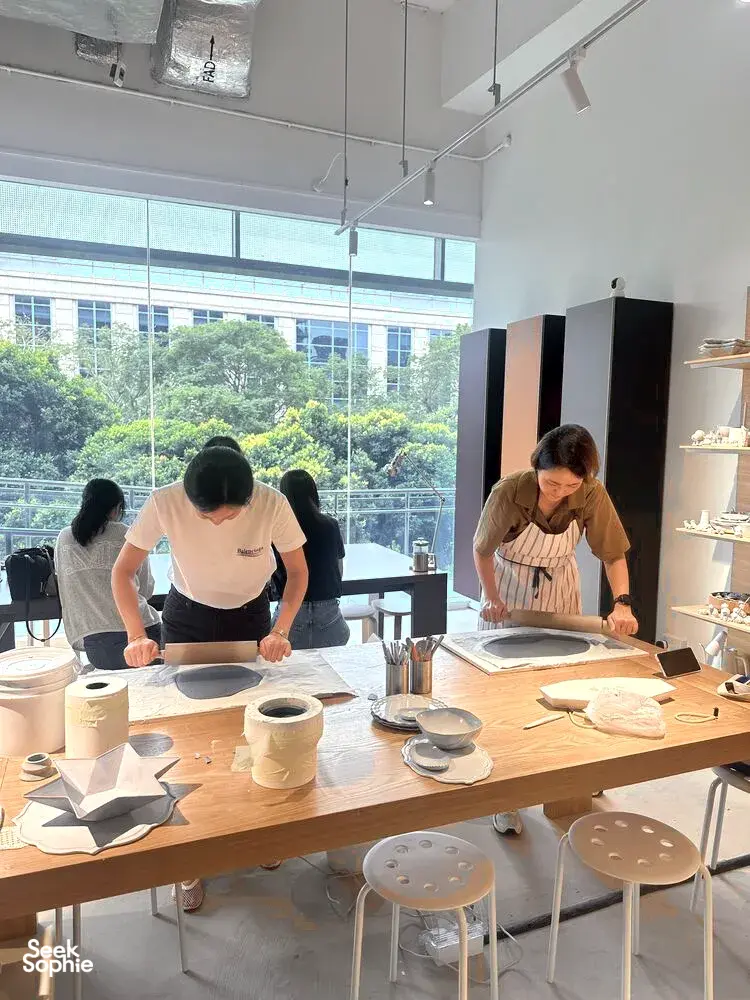 Pottery participants painting glazed ceramic pieces at Ina Atelier studio tables under large windows during workshops in Singapore