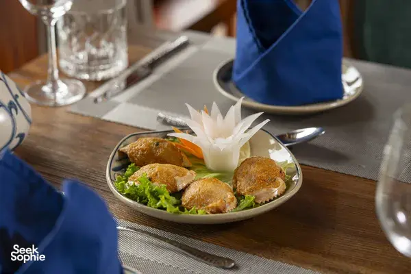 Garnished plated appetiser on a wooden dining table on a Cat Ba boutique cruise, served with utensils and tableware