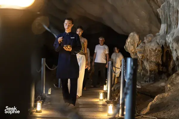 Halong Bay cave walk on a Bhaya Group luxury cruise, with guests strolling along a lantern-lit passage during an evening 3D2N itinerary