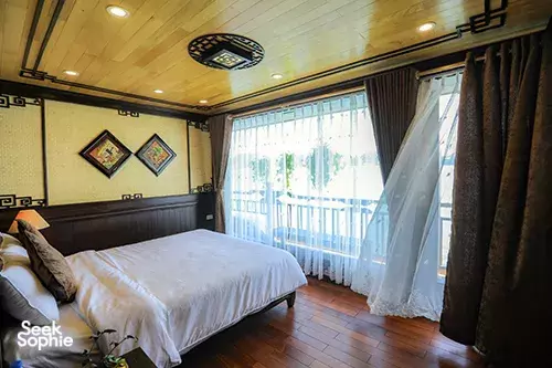 Cat Ba Ocean Cruises cabin with a double bed, wooden walls and curtains for an overnight cruise in Halong Bay