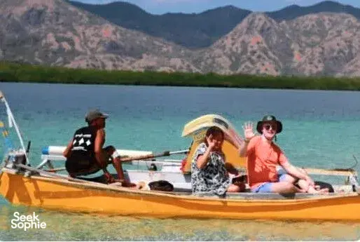 Friends seated on a small wooden boat on bright turquoise water with mountains behind them near Labuan Bajo