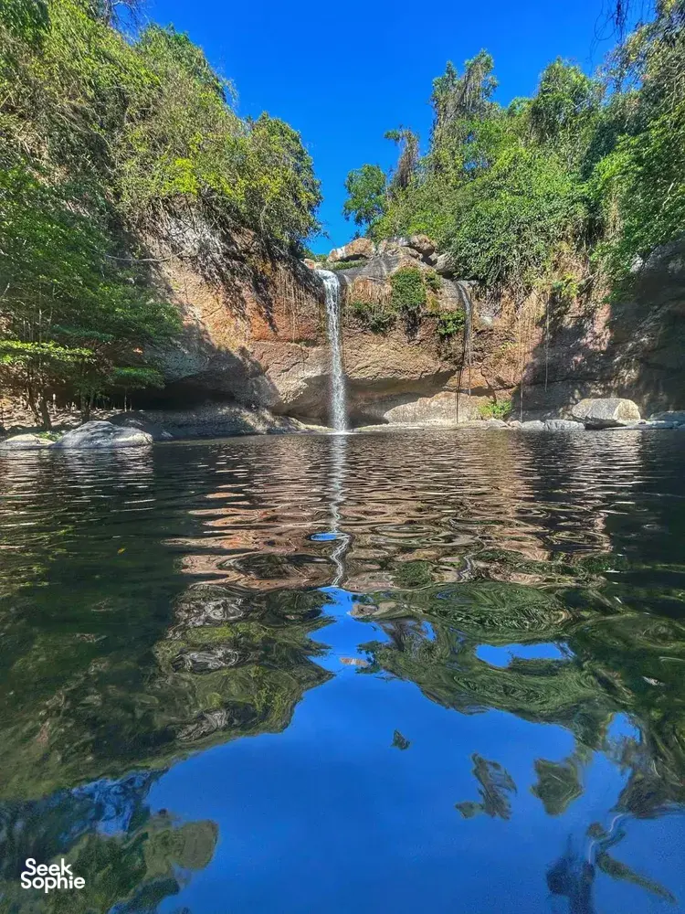 Waterfall spilling into a calm pool with reflections in Khao Yai National Park, shown during the trekking day trip