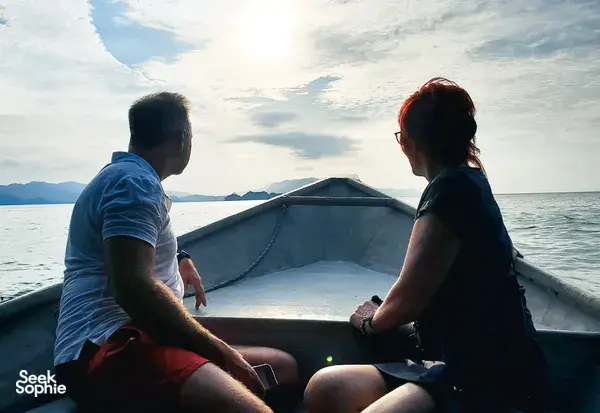 Couple relaxing at the front of a small boat during a Langkawi cruise, looking out over the sea at sunset