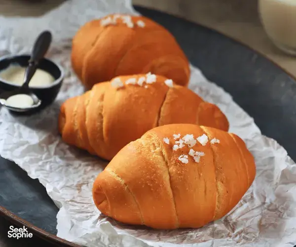 Golden shio pan buns on parchment-lined tray with a small cup of pale butter nearby, ready to bake in Singapore
