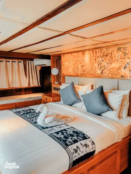 Luxurious cabin with made-up double bed and blue cushions on a Deluxe phinisi, ready for restful nights on a Komodo cruise, Labuan Bajo