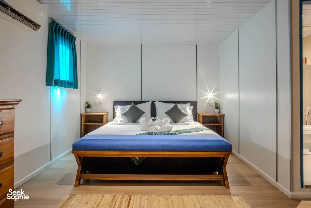 Seaventures Dive Rig cabin bedroom with air-conditioning, a neatly made bed and pillows under soft blue lighting