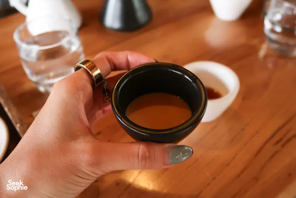 Hand holding a small cup of coffee for tasting in a family-run Lijiang workshop specialty coffee session