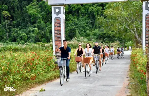 Group cycle along a quiet countryside lane with brick gateposts and garden flowers on a Cat Ba shore excursion