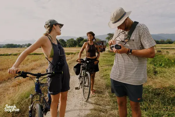 Cyclists pause on a rural Langkawi dirt path, with bikes and cameras on display, enjoying quiet island lanes