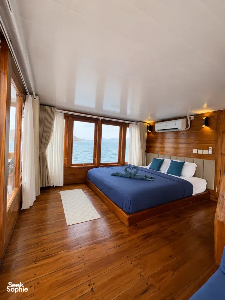 Blue-dressed beds in a wooden cabin with sea-facing windows on board the 3D2N shared Komodo cruise, Komodo Island