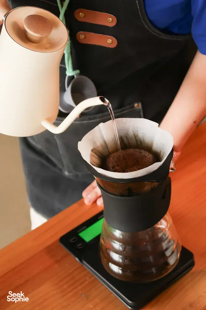 Pour-over coffee brewing: kettle pours into a filter over a dripper stand at a specialty coffee workshop in Lijiang