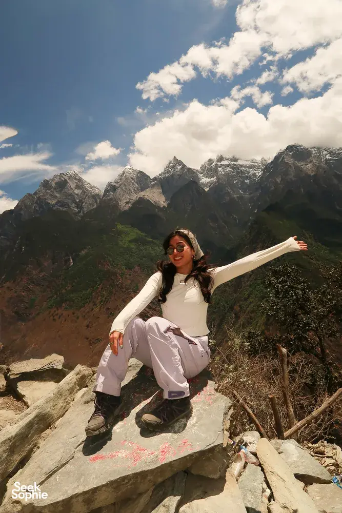 Solo hiker stretching arms on a rocky viewpoint above Tiger Leaping Gorge in Lijiang, on a 2D1N high-trail hike