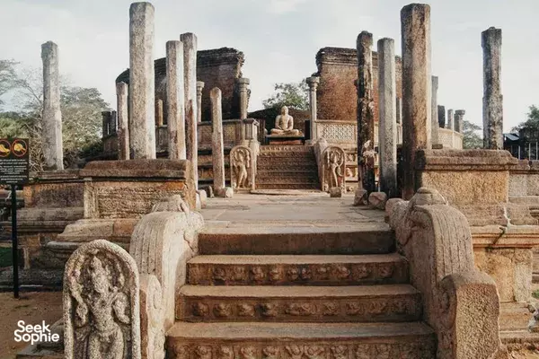 Stone temple steps with weathered pillars and carved balustrades, with a seated figure at the ancient site in Polonnaruwa
