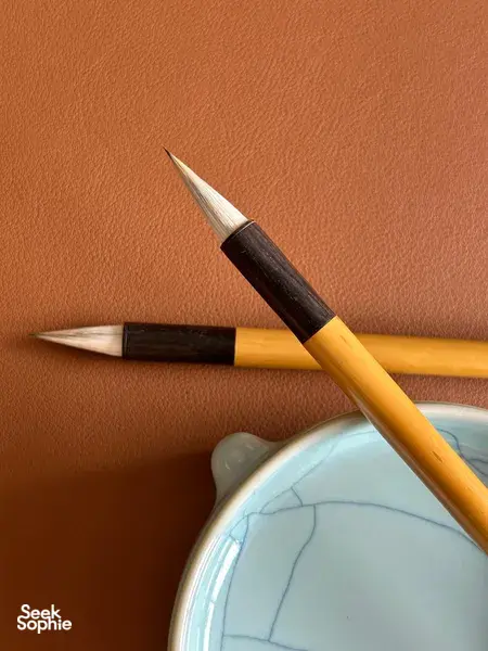 Chinese calligraphy brush tips resting on an ink stone and ceramic dish during a write-your-own blessing session—workshops in Singapore