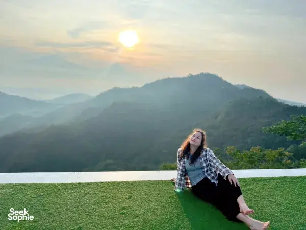 Reclining on a grassy terrace at sunrise over mountain ridges in Yogyakarta on the Picnic Indonesia-led 3-volcano coffee farm trip