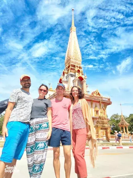 Group posing in front of a tall golden Thai temple tower on a sunny day in Phuket, with the street and sky behind