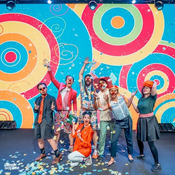 Clown troupe on a bright stage with confetti and painted scenery, posing together after games in workshops in Singapore