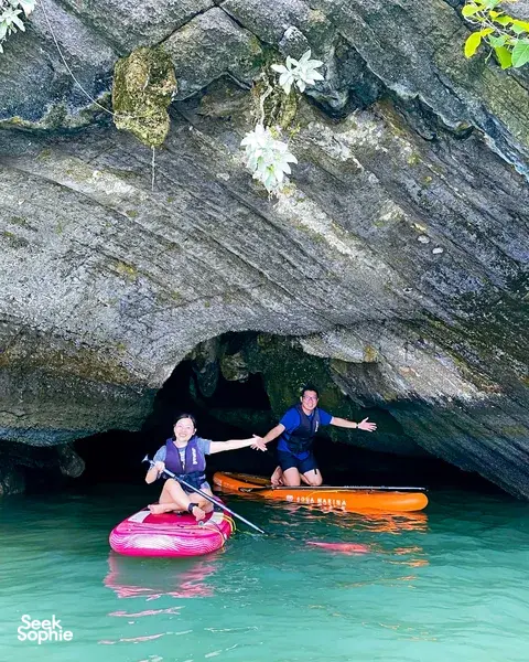 SUP riders paddling through an overhanging rock cave in turquoise water at Tanjung Rhu, Langkawi, on a guided adventure