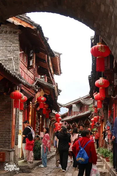 People strolling through Lijiang Old Town in a lantern-lined alley, part of a local-guided walking experience