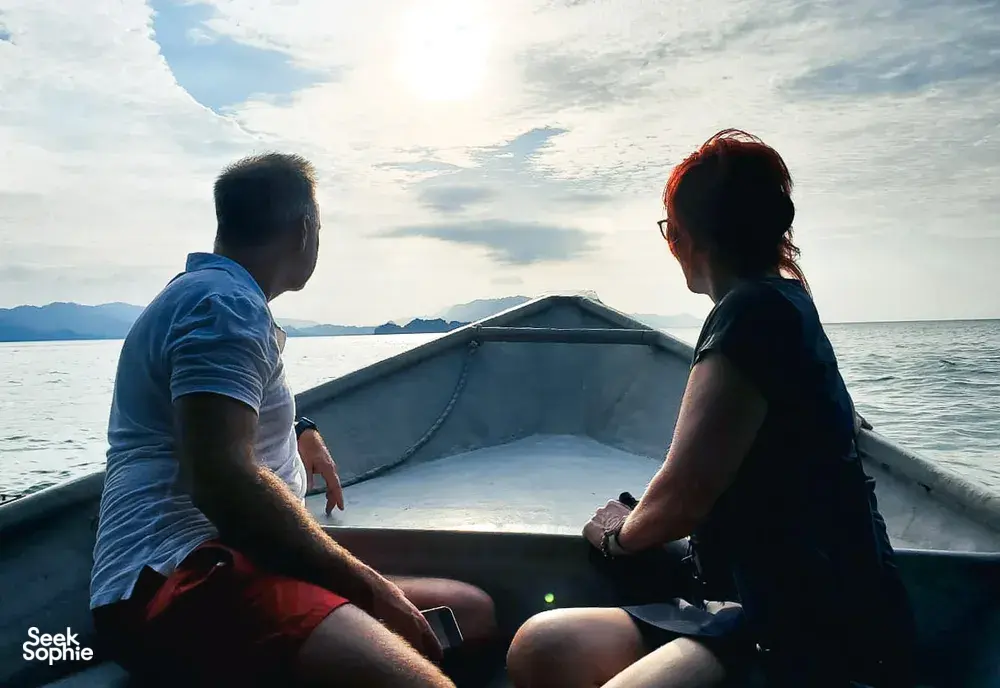 Couple relaxing at the front of a small boat during a Langkawi cruise, looking out over the sea at sunset