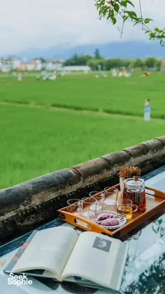 Tea set on a wooden tray beside an open book as guests unwind in the green fields near Xizhou old town, Dali