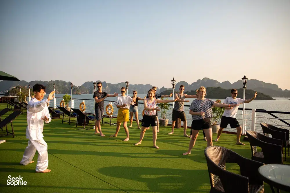 Guests performing a group stretch on a luxury cruise deck with sea views and limestone scenery in Halong Bay