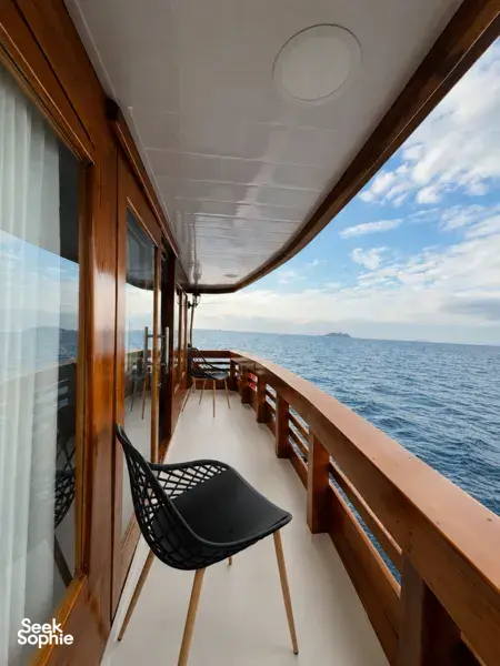 Wooden corridor on deck with a black chair and railing, opening to an ocean view on a 3D2N shared Komodo cruise, Komodo Island