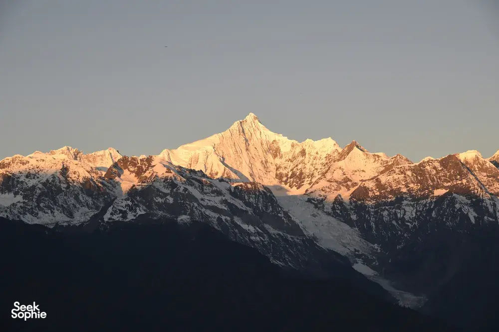 Snowy Meili Snow Mountain summit lit by early sunrise rays above dark ridgelines on a 2D2N adventure from Shangri-La