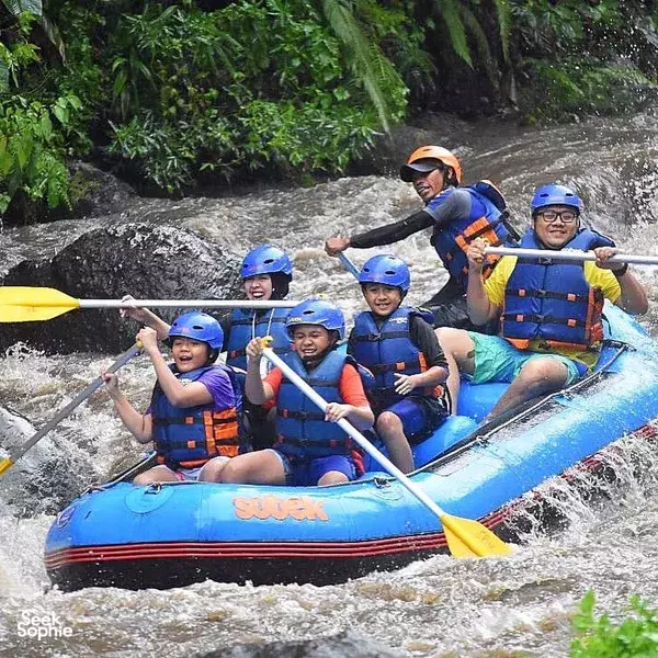Smiling rafters in helmets and life jackets paddling a blue raft through choppy water on a river in Indonesia