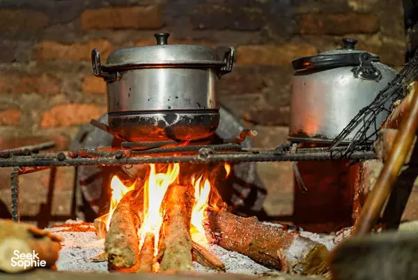 Sizzling fire cooking with large metal pots over an open flame beside stacked tools, during a foodie tour in Indonesia