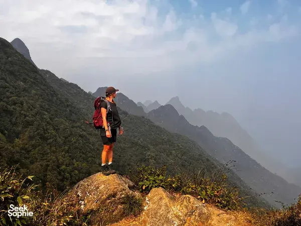Single trekker pauses on a rocky viewpoint over the Fansipan range near Sapa during an eco day hike in mountain haze