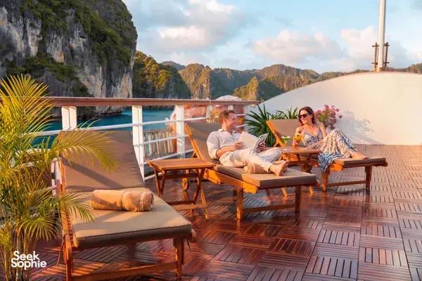 Travellers lounging on the wooden deck of a Cat Ba boutique cruise with calm bay views and limestone cliffs